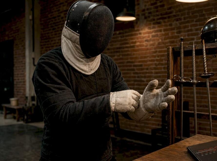 Practitioner wearing historic sword safety gear indoors